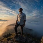 A determined man standing on a mountain peak looking at the sunrise.